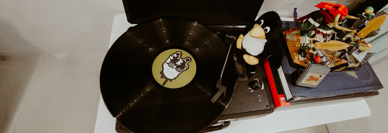 Record player spinning a vinyl record next to a Tux penguin plush, LEGO figures and a Zelda cartridge
