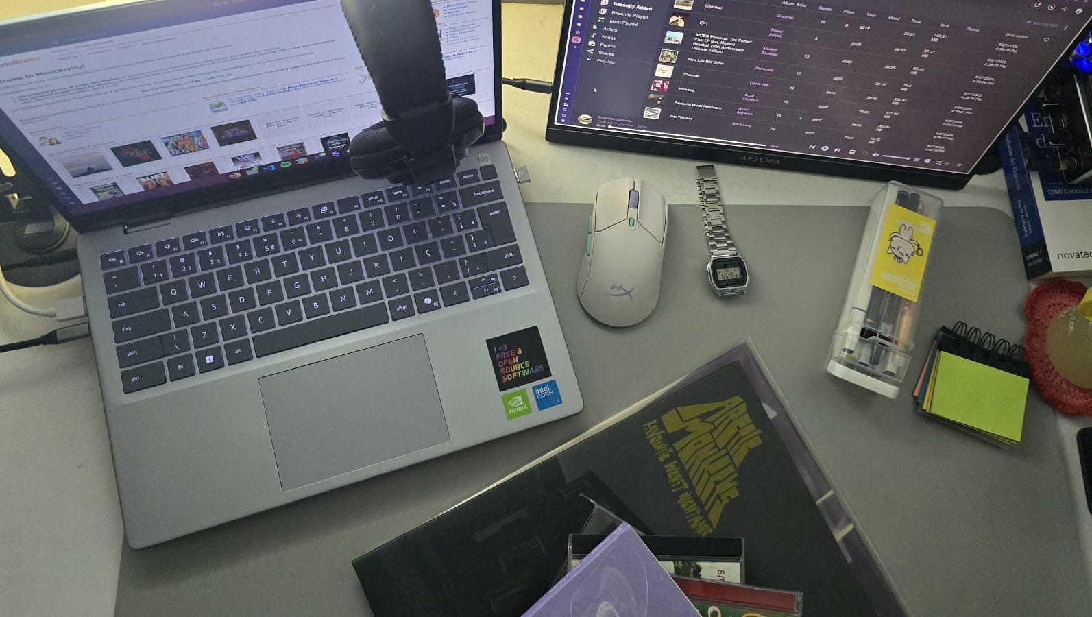 Mesa com notebook, monitor mostrando a biblioteca do Navidrome, fone de ouvido e o vinil Favourite Worst Nightmare do Arctic Monkeys