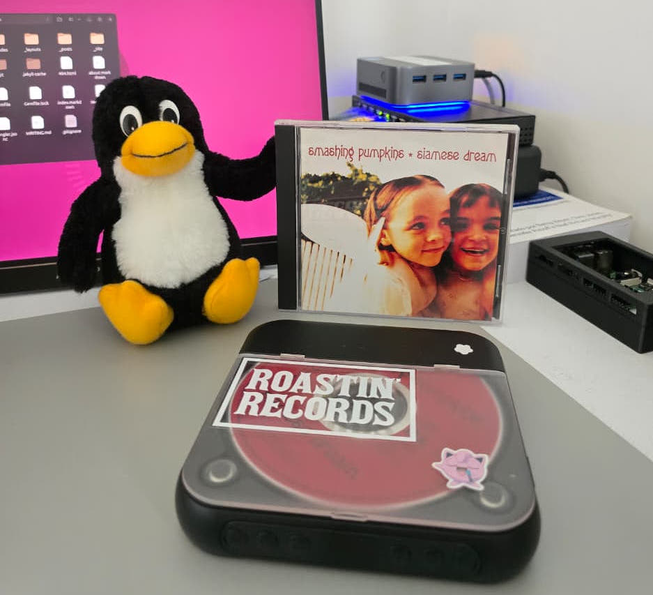 Siamese Dream CD case on a desk, next to a Tux penguin plush and a portable CD player with the red disc showing through the lid